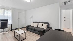 A modern, minimalistic living room with a grey sofa, a small coffee table, a TV on a stand, and a dining table. - Cozy Salt Lake Getaway - Desk w/ Monitor ! (Salt Lake City)