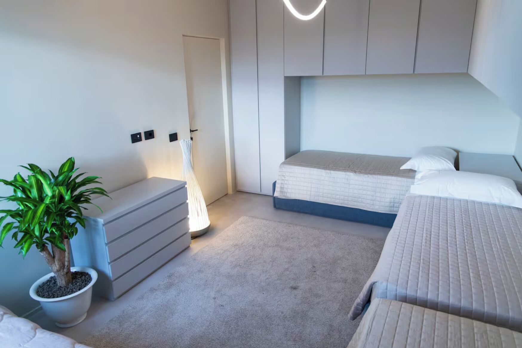 A modern bedroom with a bed, bedside tables, a potted plant, and a lamp.