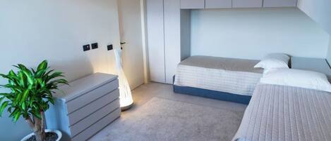 A modern bedroom with a bed, bedside tables, a potted plant, and a lamp.