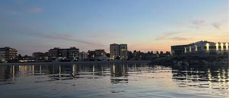 A waterfront cityscape with buildings reflecting on calm water.