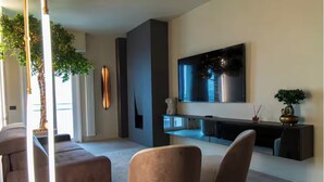 A modern living room with a large TV, comfortable seating, a plant, and a fireplace. - Super Beachfront Penthouse for Families with Breakfast, 2 Parking Spaces, Private Beach (Fano)