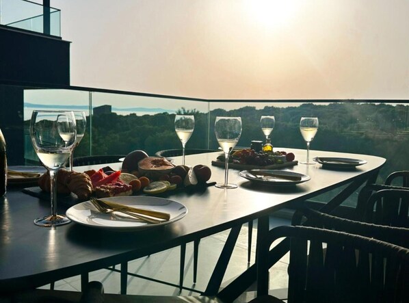 A dining table set with wine glasses, plates, and food, overlooking a scenic landscape.