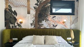 A hotel room with a bed, two pillows, a green headboard, a wall mural, a TV, and two bedside tables with lamps.