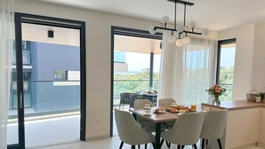 Ein modernes Esszimmer mit einem für das Frühstück gedecktem Tisch, großen Fenstern mit Vorhängen und Blick nach draußen.