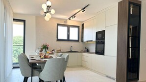 Eine moderne Küche mit weißen Schränken, einem Esstisch mit Stühlen, einer Deckenleuchte und einem großen Fenster.