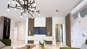 Ein modernes Wohnzimmer mit rundem Couchtisch, einer Couch, einem an der Wand befestigten Fernseher und einer dekorativen Pendelleuchte.