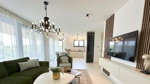 Ein modernes Wohnzimmer mit einem grünen Sofa, einem weißen Couchtisch und einem großen Flachbildfernseher an der Wand.