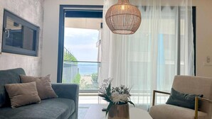 A modern living room with a grey sofa, a beige armchair, a white coffee table, and a hanging light fixture. - One-Bedroom Apartment With Terrace (The Sunset One) -S2 (Kozino)