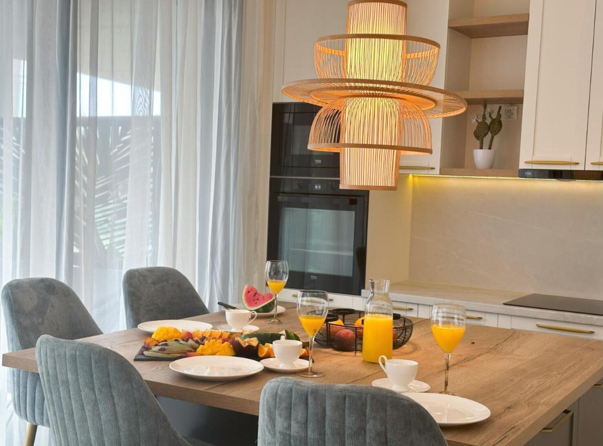 A modern dining area with a wooden table set for breakfast, featuring fruit and orange juice.