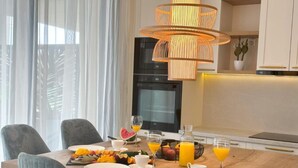 A modern dining area with a wooden table set for breakfast, featuring fruit and orange juice. - One-Bedroom Apartment With Terrace (The Sunset One) -S2 (Kozino)