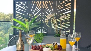 A table set with a bottle of champagne, wine glasses, a cheese board with grapes, and a pitcher of orange juice. - One-Bedroom Apartment With Terrace (The Sunset One) -S2 (Kozino)