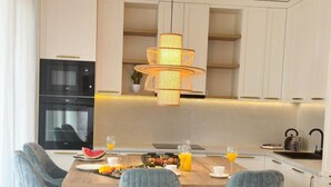 A modern kitchen with a central island, built-in appliances, and a hanging light fixture. - One-Bedroom Apartment With Terrace (The Sunset One) -S2 (Kozino)