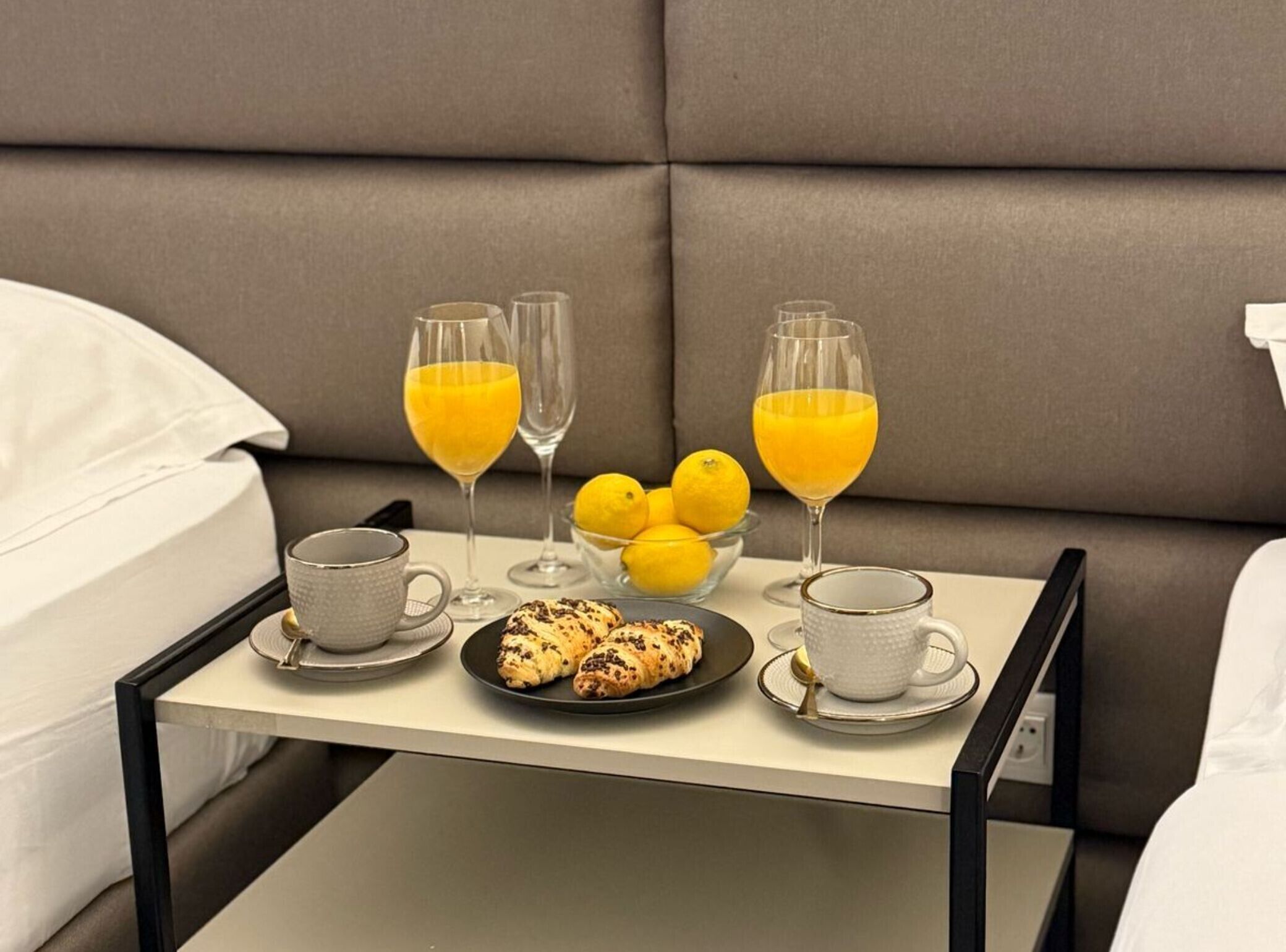 A neatly arranged breakfast tray on a bed with a grey upholstered headboard.