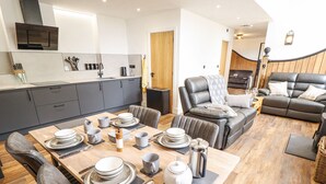 Une cuisine moderne avec des meubles de couleur gris foncé, une table à manger en bois pour quatre personnes et un canapé en cuir dans l’espace salon.