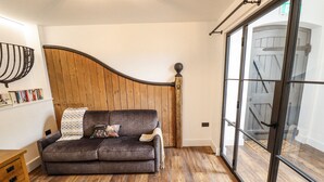 Un salon moderne avec un canapé gris, un mur recouvert de panneaux en bois et une grande porte en verre donnant sur un escalier en bois.