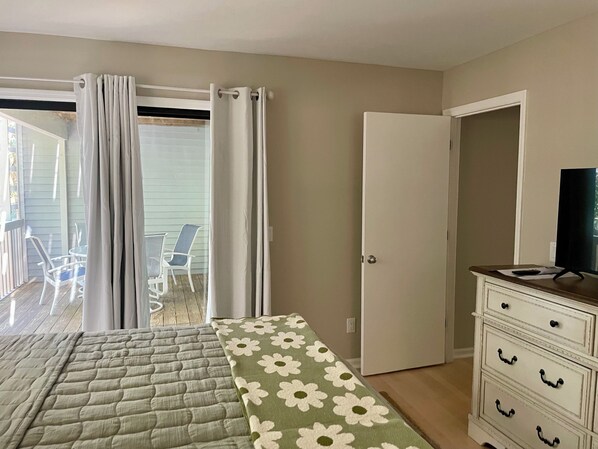 Un dormitorio con una cama, un aparador, un televisor y un ventanal corredera que da a un balcón con sillas.
