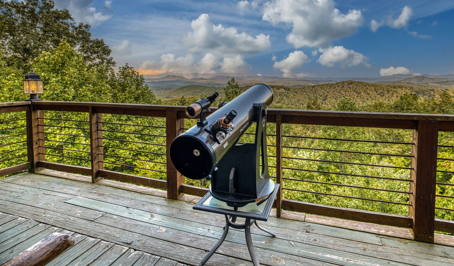 A telescope on a wooden deck with a view of a mountainous landscape.