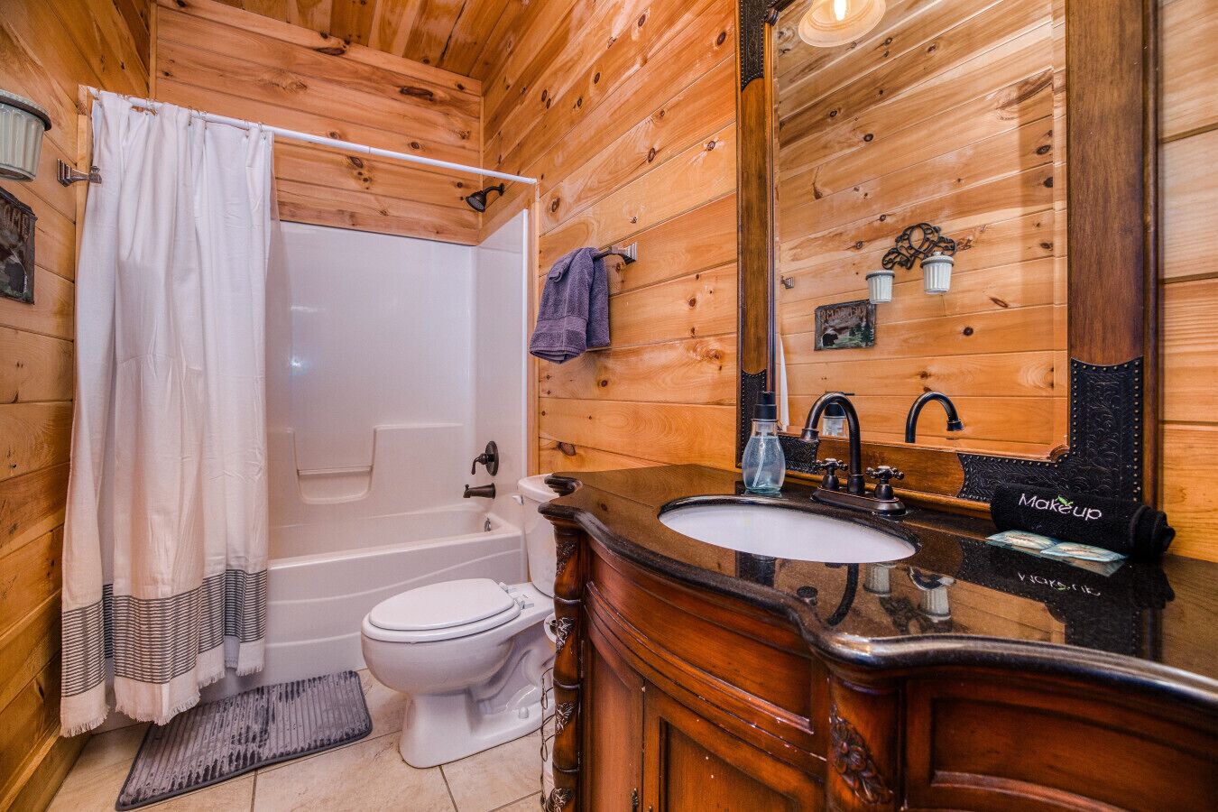 A wooden cabin bathroom with a bathtub, toilet, and vanity with a sink and mirror.