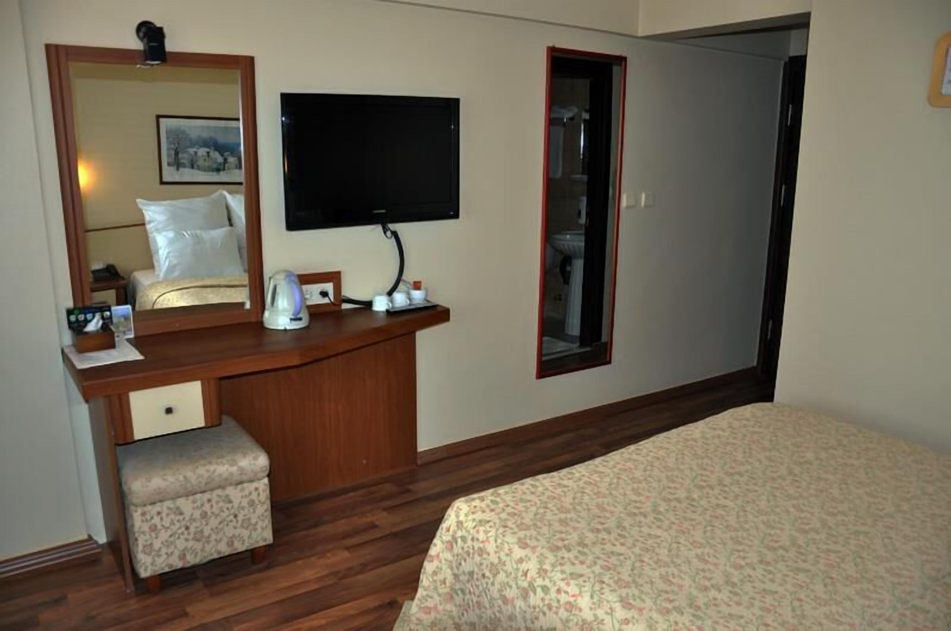 A hotel room with a bed, a wooden desk with a chair, a television, and a mirror.