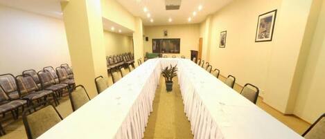 Un salón de conferencias con una larga mesa, sillas y una pantalla de proyector.