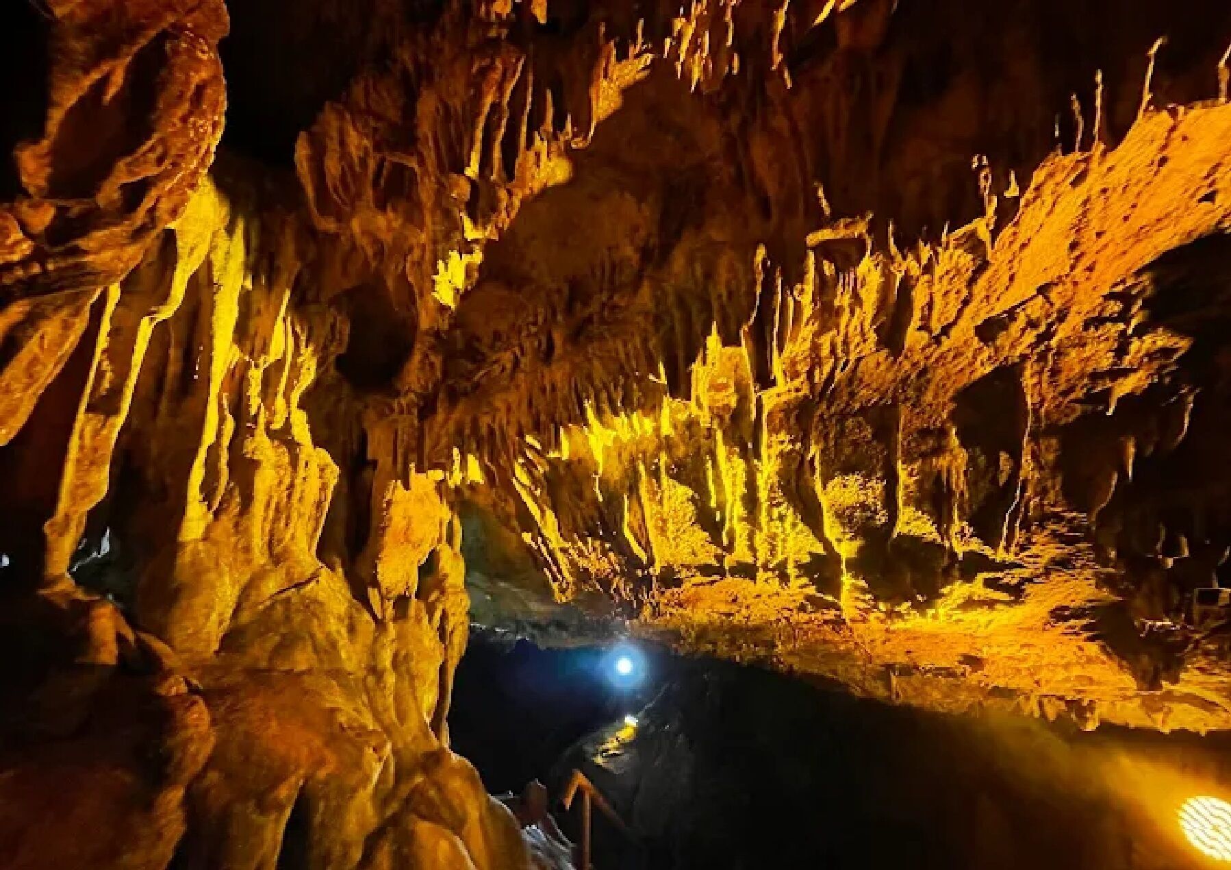 A cave with stalactites and stalagmites illuminated by artificial lighting.