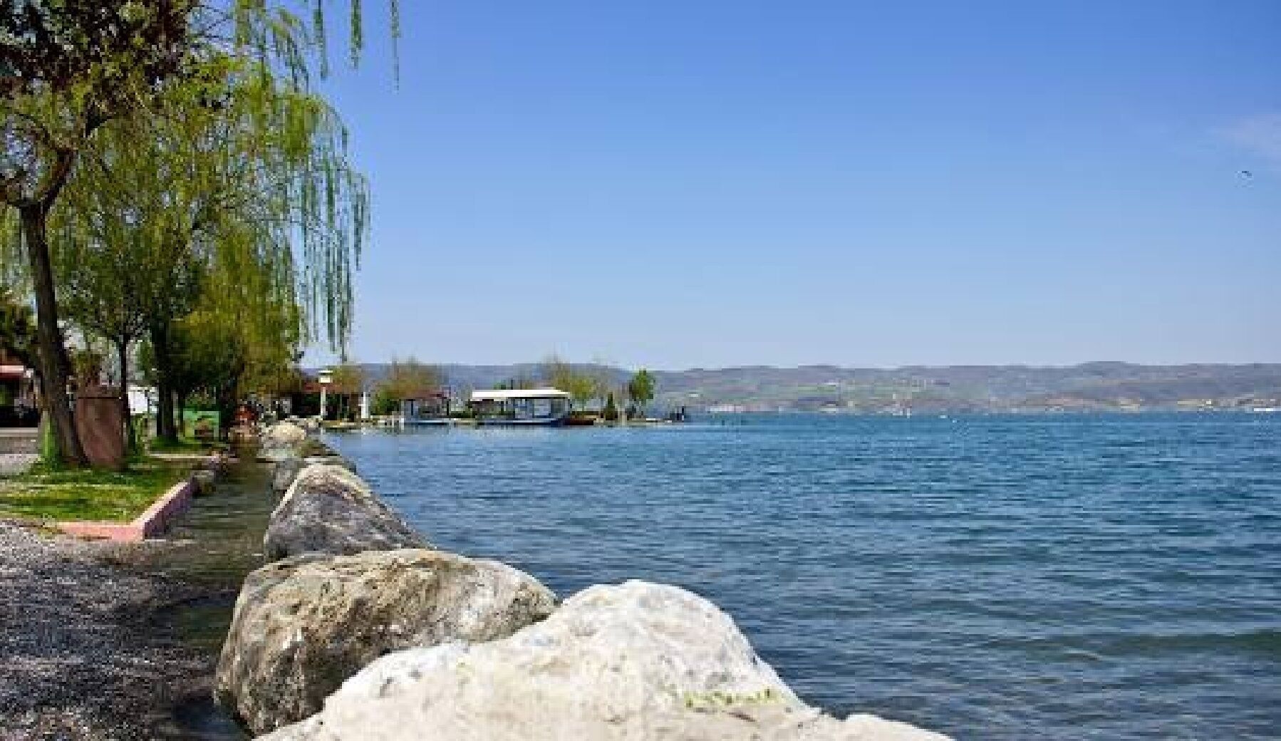 Vista de un lago con un muelle, agua tranquila y una orilla distante.