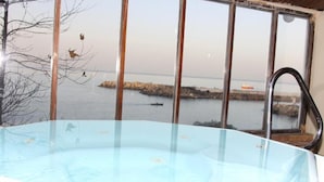 Une piscine à fond de verre offrant une vue sur une côte rocheuse et un navire au loin.