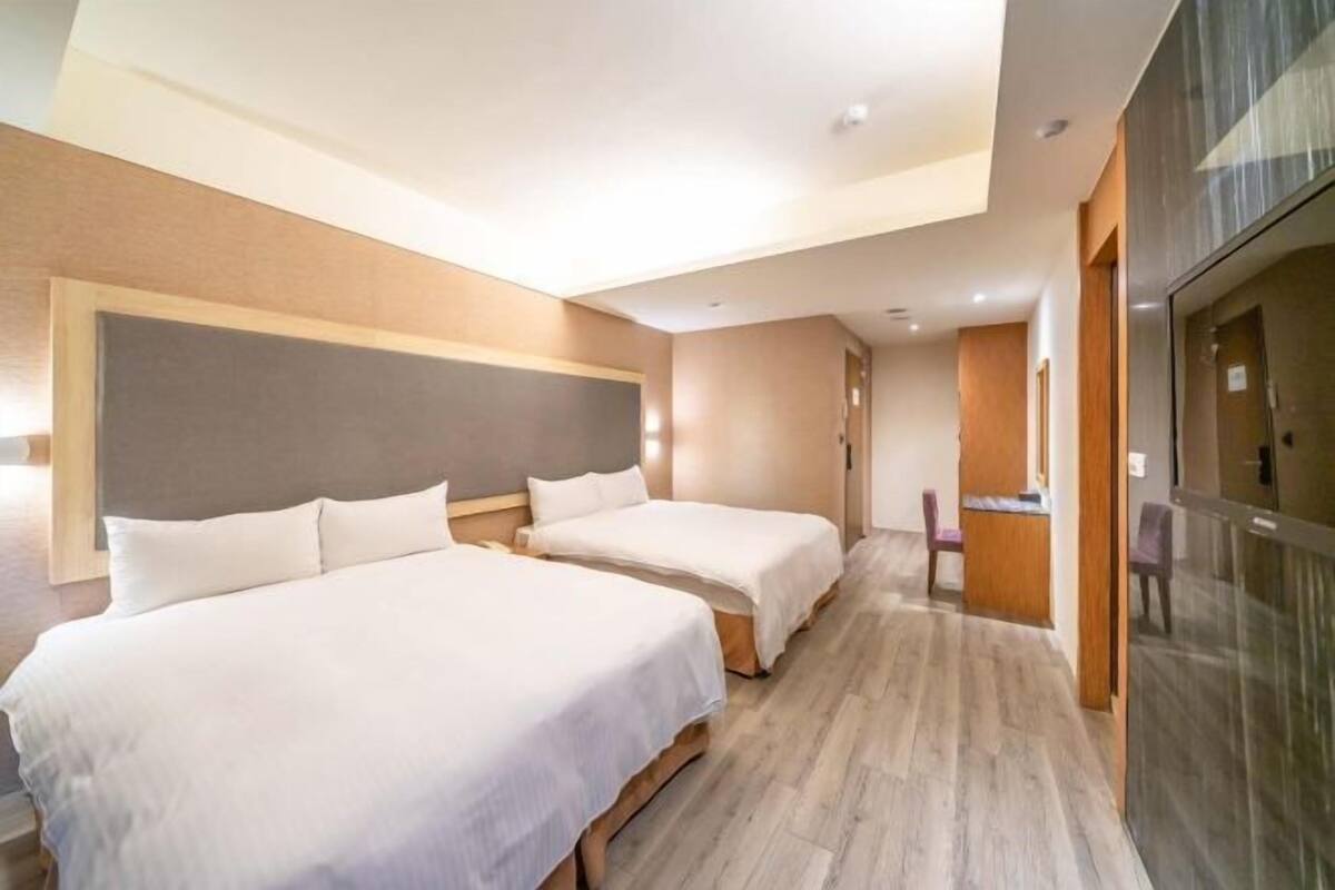 A hotel room with two beds, a wooden floor, a large window, and a reception desk.
