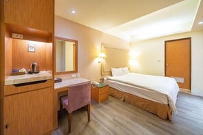 A hotel room with a bed, desk, chair, and a mirror.