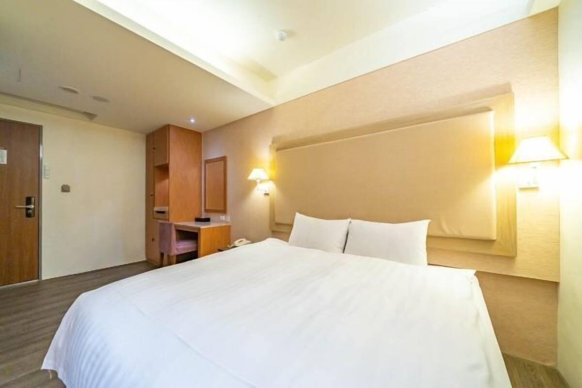 A hotel room with a large bed, a desk, a mirror, and two bedside lamps.