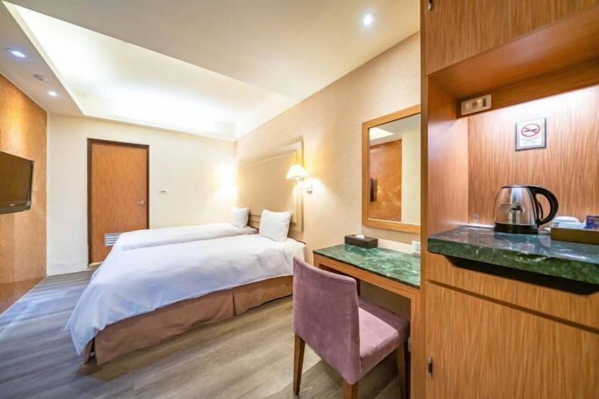 A hotel room with two beds, a desk with a chair, a mirror, a coffee maker, and a television on the wall.