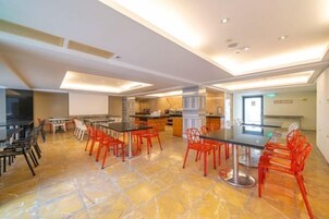 Un comedor amplio con sillas rojas y una mesa grande, una zona de cocina con electrodomésticos modernos, y un techo bien iluminado con focos empotrados.