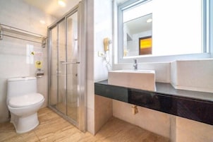 Un baño con inodoro, cabina de ducha de vidrio, lavabo con espejo y ventana.