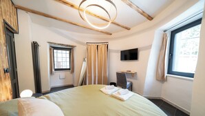 A hotel room with a large bed, a flat-screen TV mounted on the wall, a window with curtains, and a ceiling light fixture.