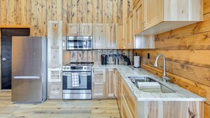 A modern kitchen with wooden paneling, stainless steel appliances, and a marble countertop. - Hunt, Fish & Boat: Northwoods Hideaway (Tomahawk)