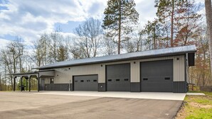 A large industrial building with multiple garage doors, a covered loading dock, and a paved driveway. - Hunt, Fish & Boat: Northwoods Hideaway (Tomahawk)