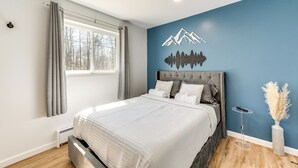 A bedroom with a large bed, a window with curtains, a wall-mounted artwork of mountains, and a bedside table with a vase. - Poconos Hot Tub Haven! 14 Mi to Camelback Resort (Coolbaugh Township)