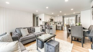 A modern living room with a grey sofa, ottoman, and dining area with grey chairs. - Poconos Hot Tub Haven! 14 Mi to Camelback Resort (Coolbaugh Township)
