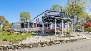 A two-story house with a covered porch, stone retaining wall, and a small garden area with outdoor seating. - Waterfront Home w/ Deck on Lake Carmel (Carmel Hamlet)