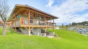 Casa de madera de dos pisos con balcón, cimientos de piedra y vista a un paisaje montañoso.