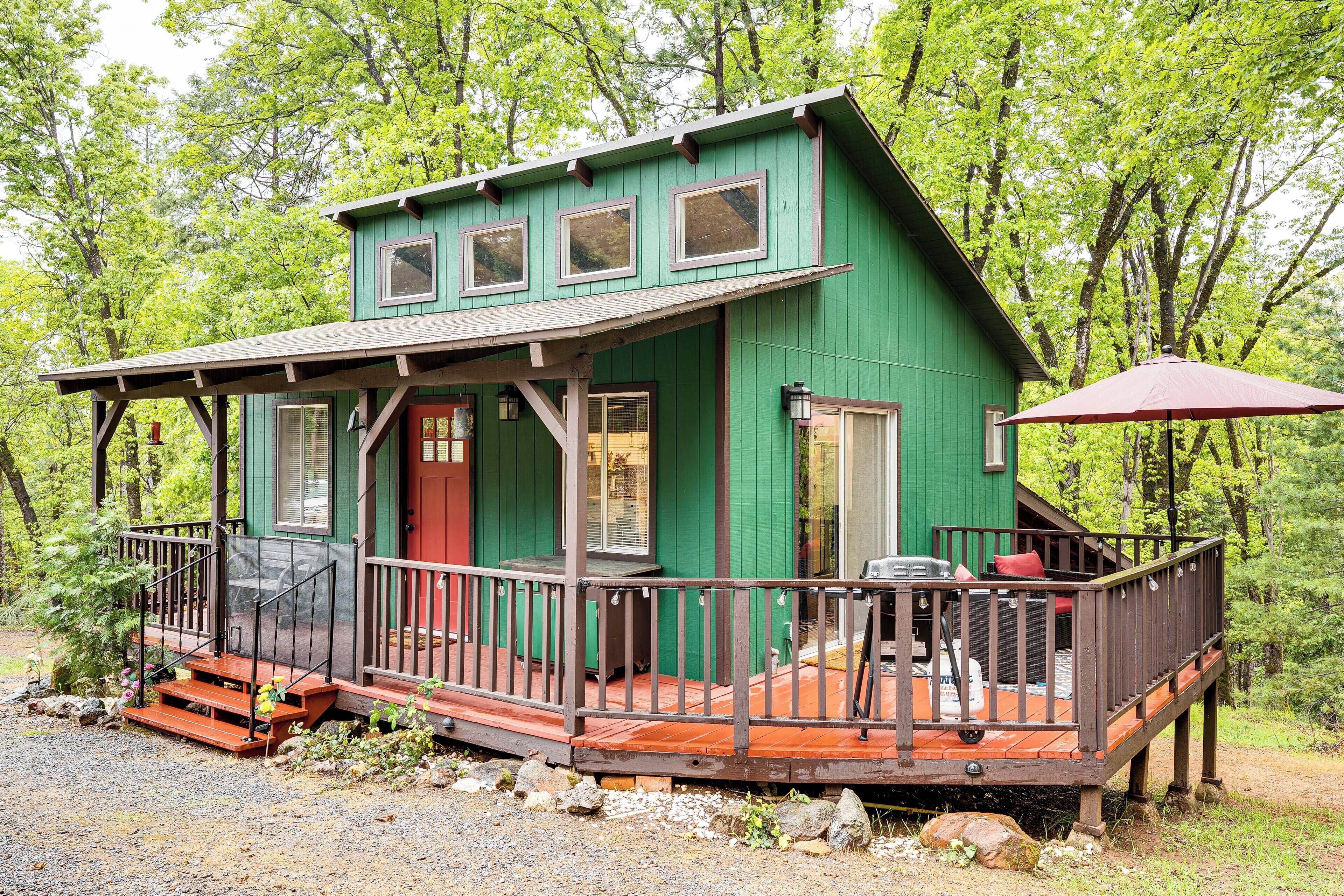 A green cabin with a wooden deck, a covered porch, and a red door.
