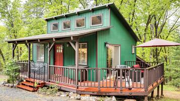 A green cabin with a wooden deck, a covered porch, and a red door.