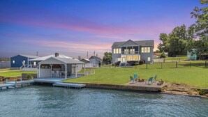 A waterfront property with a dock, a small building with a porch, and a larger house with a balcony. - Lakefront Getaway with Dock, Pool, Sunset Games (Greenwood)