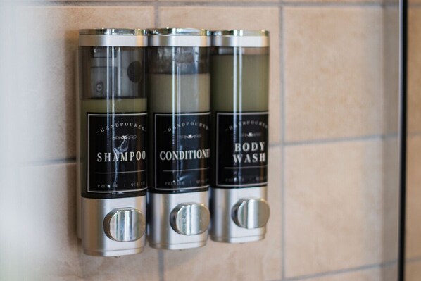 Three metallic dispensers labeled "Shampoo," "Conditioner," and "Body Wash" mounted on a tiled wall. - Lakefront Getaway with Dock, Pool, Sunset Games (Greenwood)