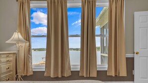A bedroom with a large window, a bed, a dresser, and a lamp. - Lakefront Getaway with Dock, Pool, Sunset Games (Greenwood)