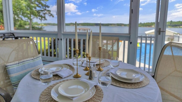 A table set for four with candles, glasses, and plates, overlooking a lake and pool. - Lakefront Getaway with Dock, Pool, Sunset Games (Greenwood)