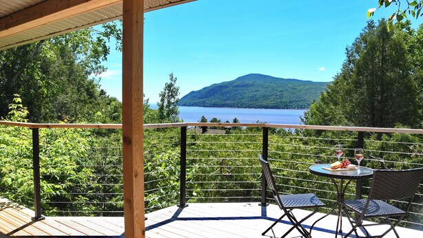 Una terraza de madera con una mesa y sillas, con vistas a un lago y una montaña.