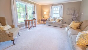 A spacious living room with a beige carpet, two sofas with patterned cushions, a small side table, and a lamp.
