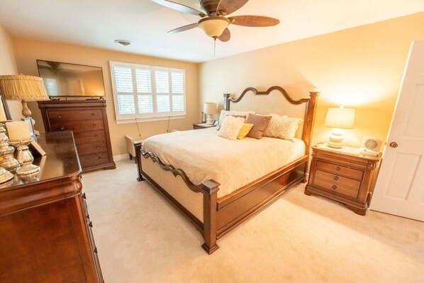 A bedroom with a wooden bed, a ceiling fan, a dresser, a nightstand, and a lamp.