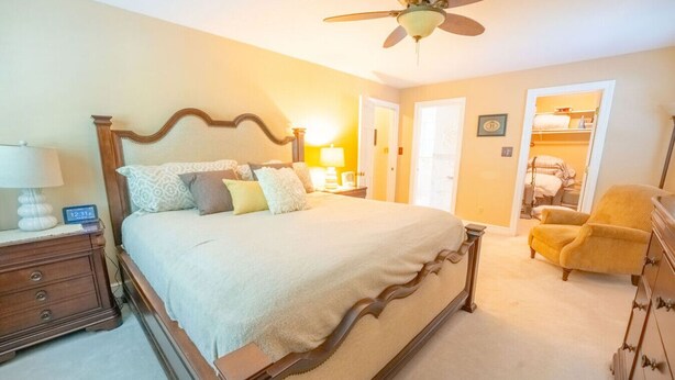 A bedroom with a large bed, a nightstand with a lamp, a chair, and a dresser.